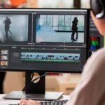 Une femme portant un casque travaille sur un logiciel de montage vidéo, affiché sur un écran avec des séquences, une timeline et des outils d'édition, dans un environnement lumineux.